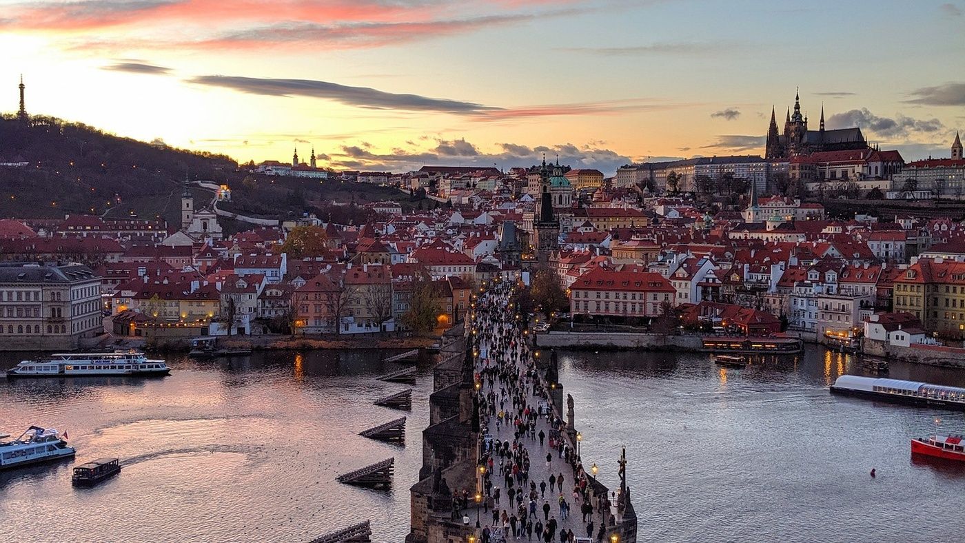 Vivid Sunset at Charles Bridge: Experience the magic of a vivid sunset at the historic Charles Bridge in Prague. As the sun dips below the horizon, the bridge comes alive with the movement of people, their silhouettes adding to the enchanting atmosphere. The warm, golden lights along the bridge and the city's skyline create a stunning contrast against the deepening twilight. This picturesque scene captures the timeless beauty and romantic allure of Prague, making it an unforgettable moment for all who visit