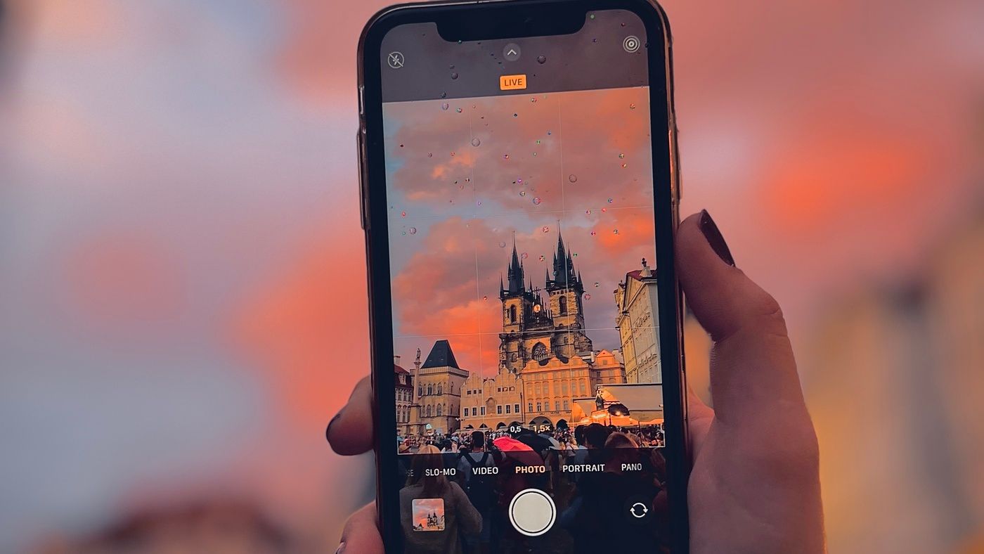 Capturing the Beauty of Old Town Square in the Rain: A mesmerizing view of Prague's Old Town Square at sunset, as seen through the lens of an iPhone camera held by a female hand. Raindrops create a captivating visual effect, enhancing the charm of this historic square. The soft, colorful hues of the sunset contrast beautifully with the rain-slicked cobblestones. This unique perspective captures the essence of Prague's romantic allure even in wet weather.
