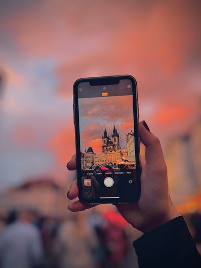  Capturing the Beauty of Old Town Square in the Rain: A mesmerizing view of Prague's Old Town Square at sunset, as seen through the lens of an iPhone camera held by a female hand. Raindrops create a captivating visual effect, enhancing the charm of this historic square. The soft, colorful hues of the sunset contrast beautifully with the rain-slicked cobblestones. This unique perspective captures the essence of Prague's romantic allure even in wet weather.